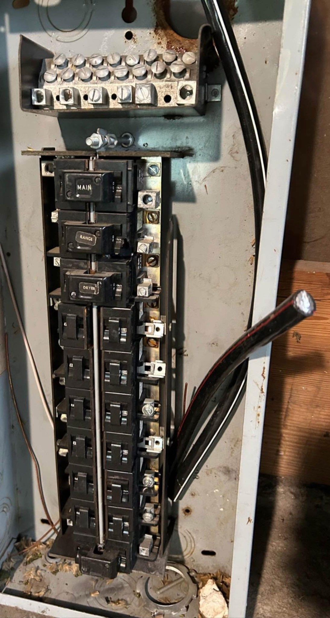 An open electrical panel box with breakers, metal bus bars, and a thick black wire protruding from the side.