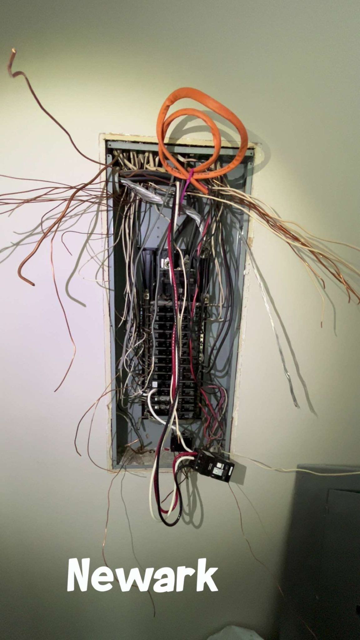 An open electrical panel in a wall with numerous loose, multi-colored wires hanging out and 
