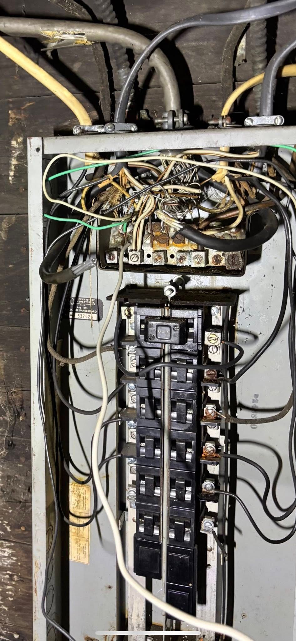 Open electrical breaker panel with a dense, messy tangle of black and white wiring inside a metal enclosure.