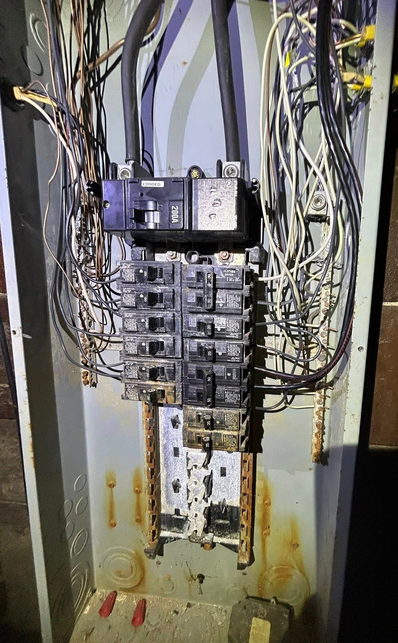 An electrical panel showing signs of corrosion and rust, with wires connected to circuit breakers.