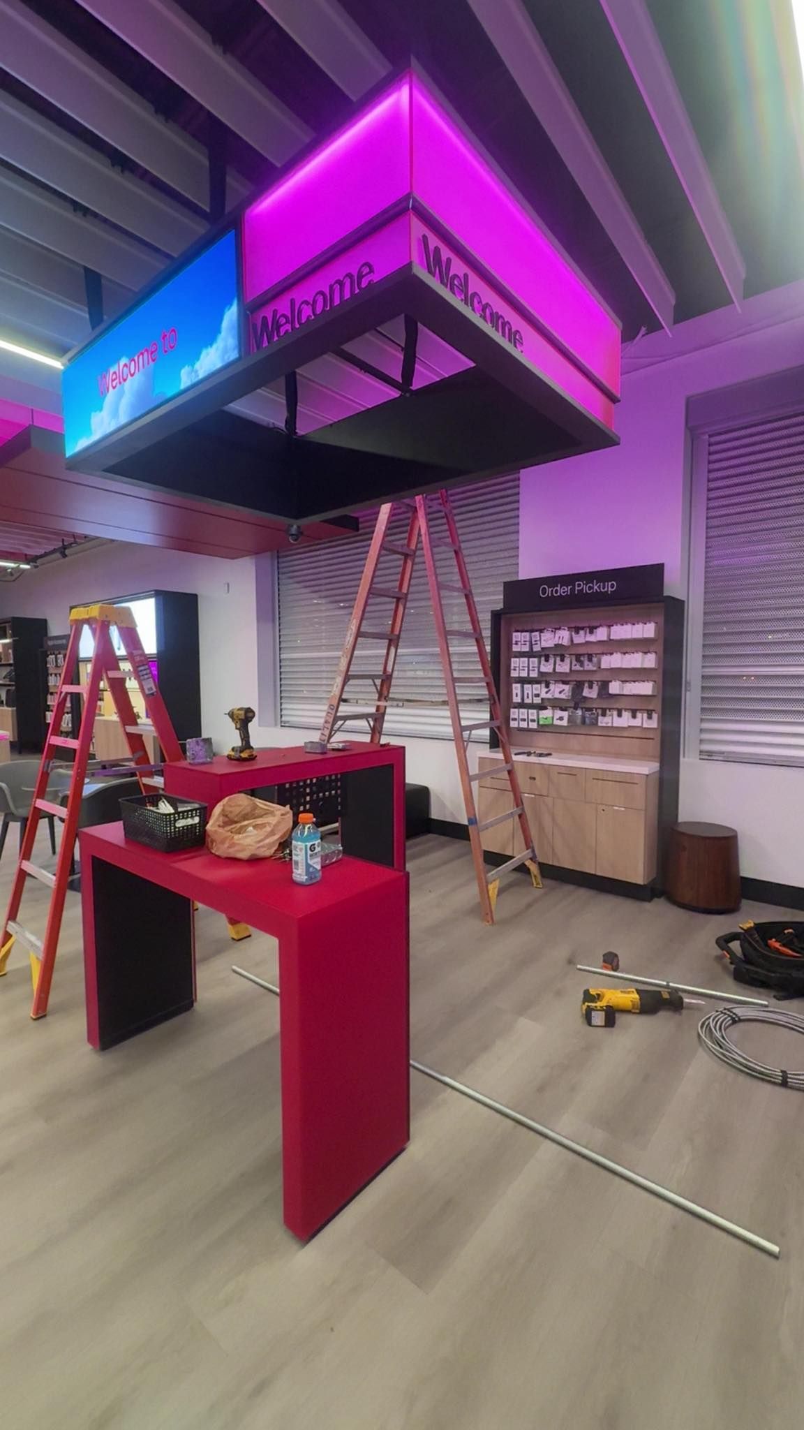 Interior view of an office space under construction, featuring a magenta, illuminated, suspended sign above a matching desk.