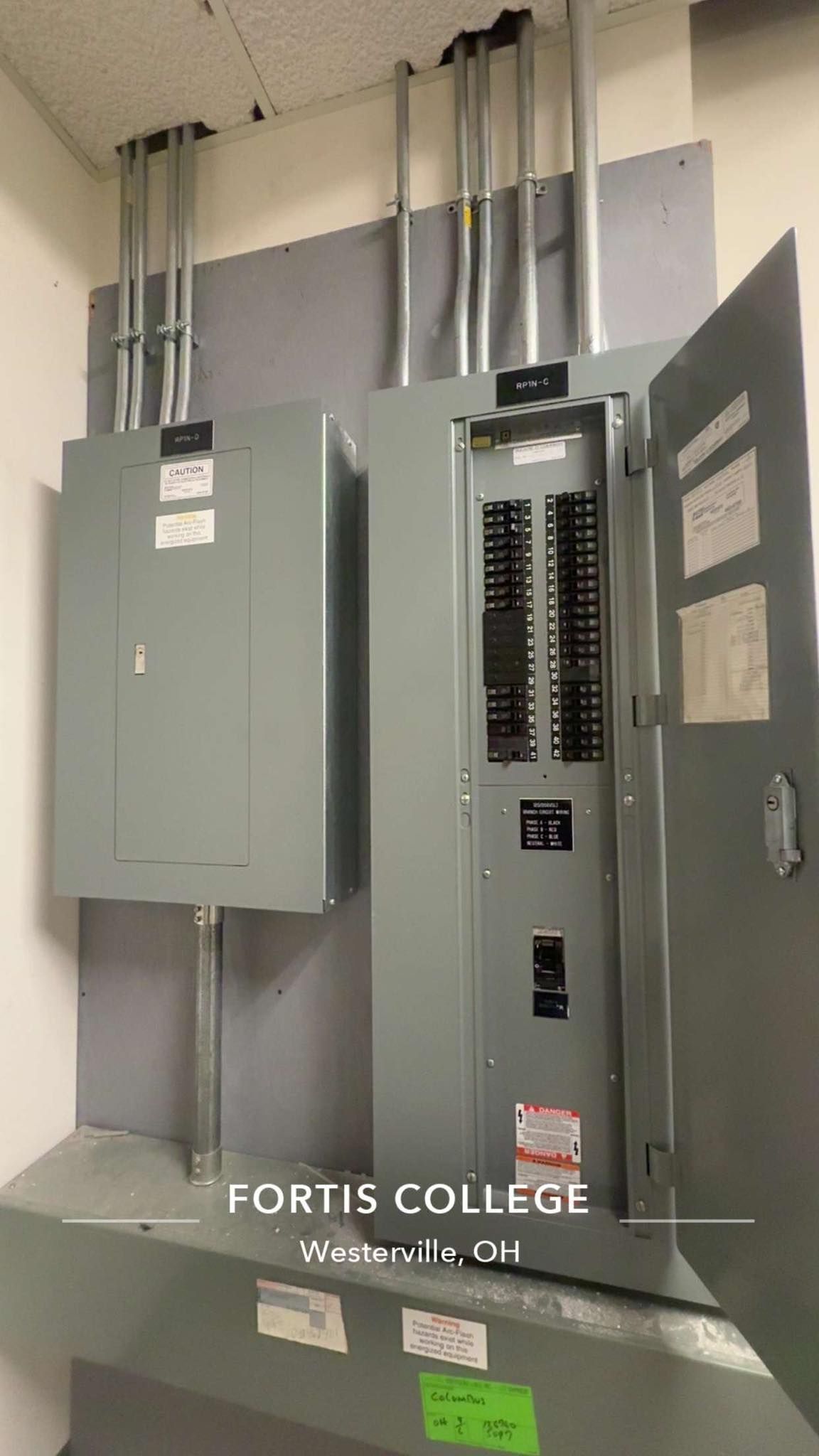 Two gray electrical panel boxes mounted on a wall with conduit piping extending through the ceiling.