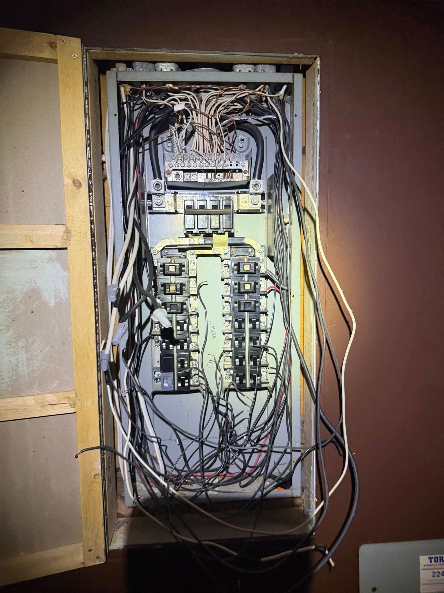 An open electrical service panel showing a dense, disorganized collection of wires connected to circuit breakers.