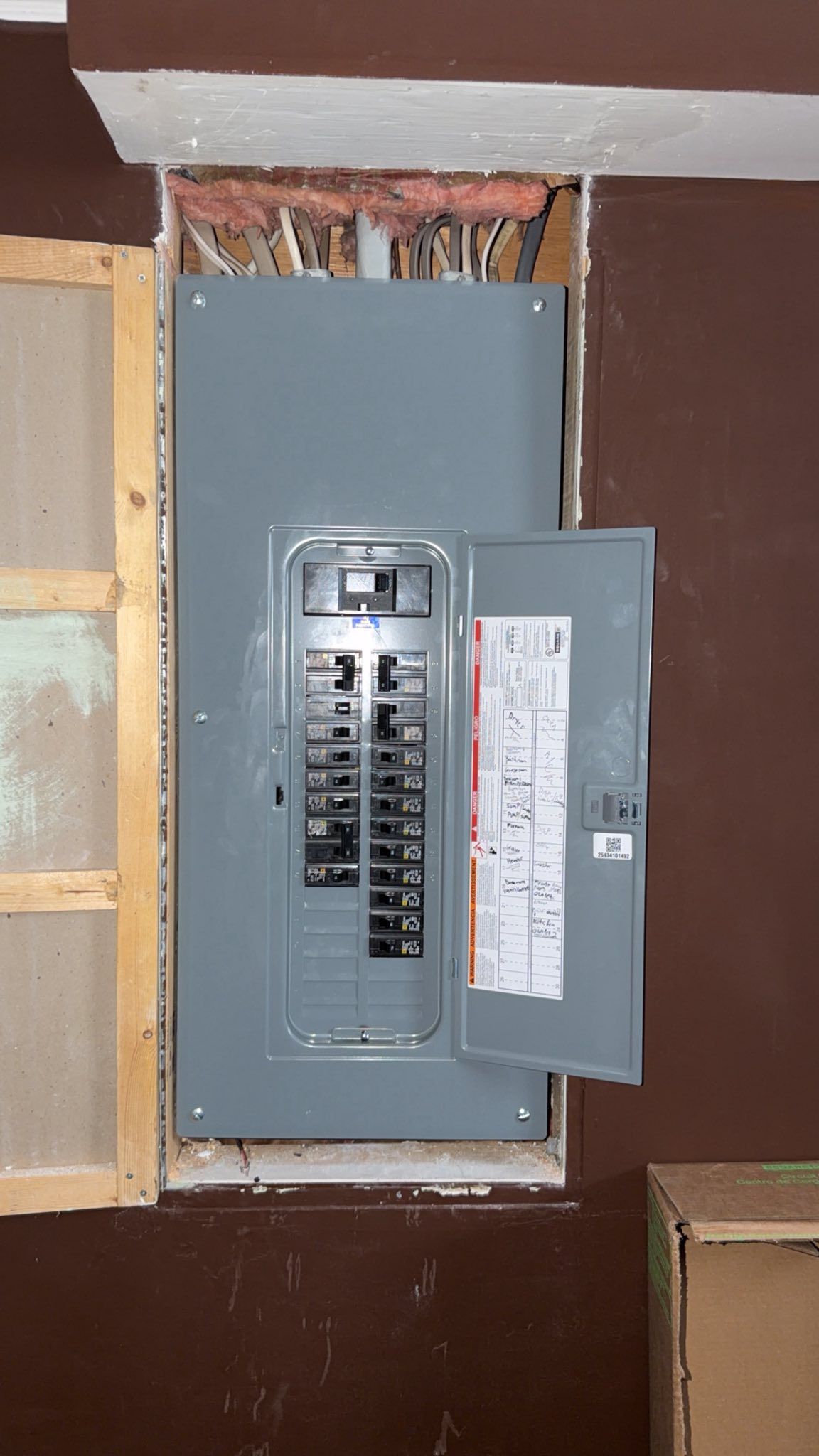 An electrical breaker panel set into a brown wall, with a door open to reveal the switches and wiring visible above.