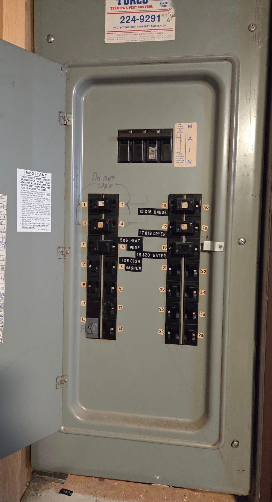 An open grey electrical service panel with a main breaker at the top and several branch circuit breakers below.