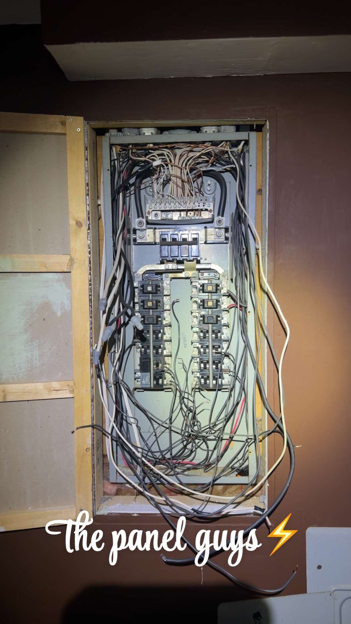 An open electrical service panel showing extensive wiring and circuit breakers, with 