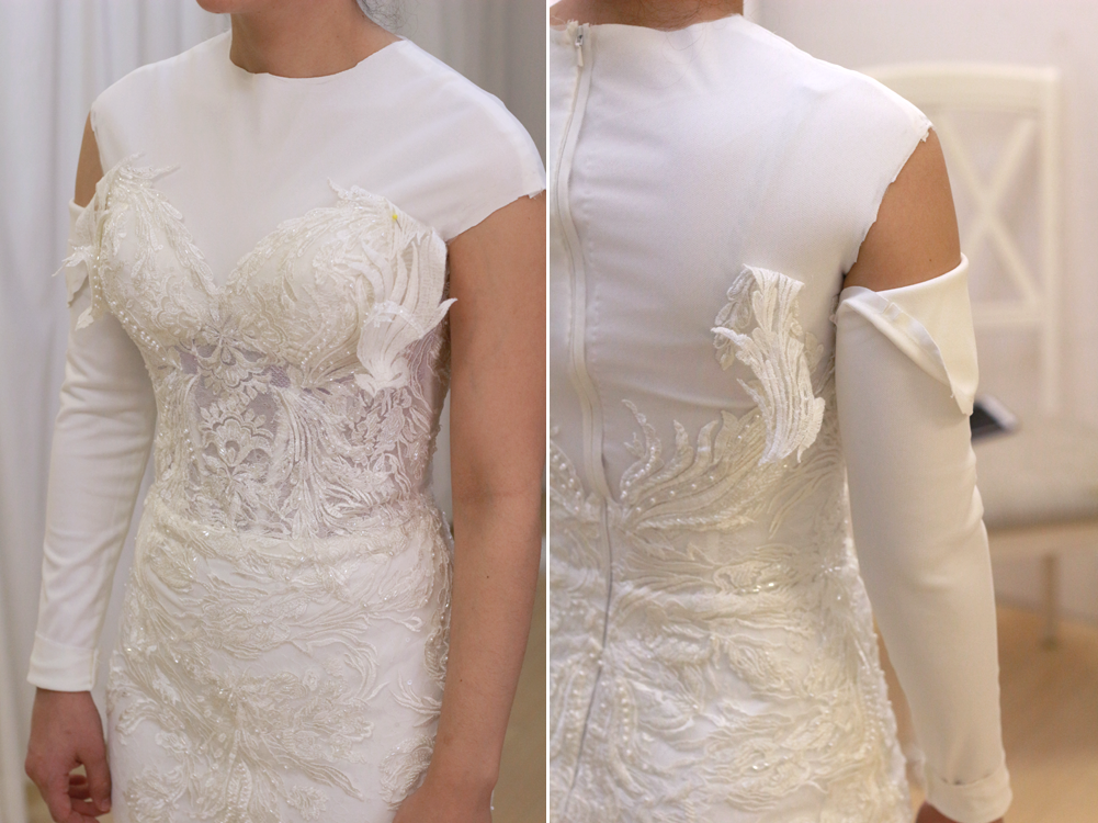 Woman in a white wedding dress with lace bodice, one long sleeve, the other with a cutout, in a room.
