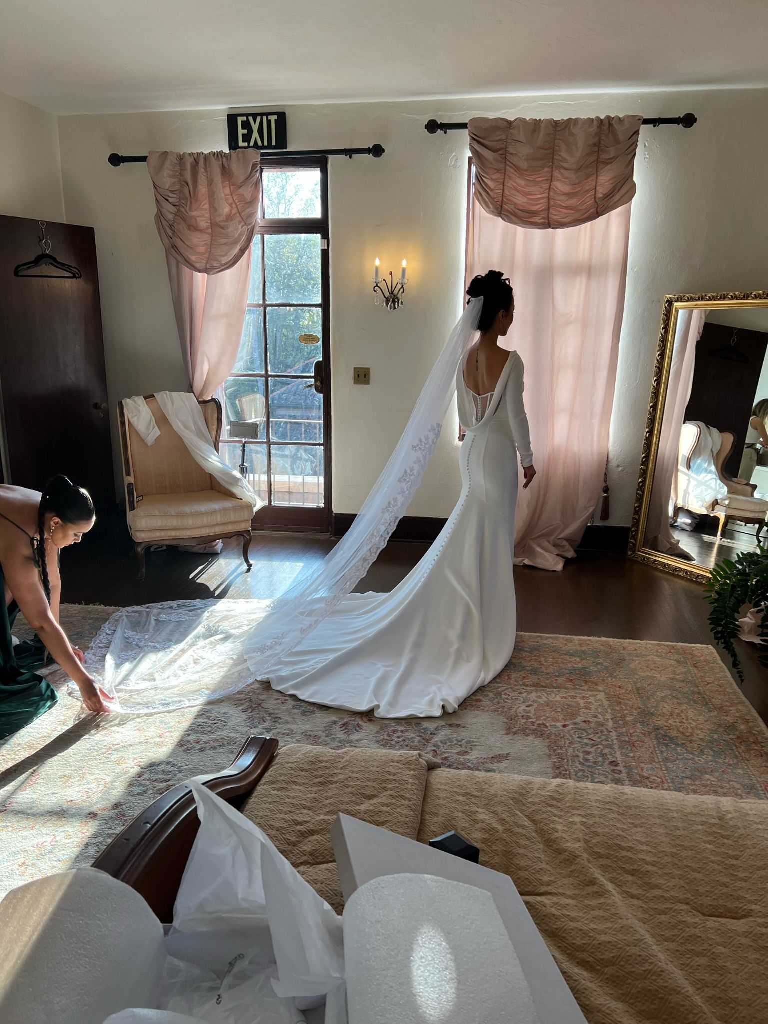 Bride in a wedding dress, train spread, posing in room with mirror and sunlight.