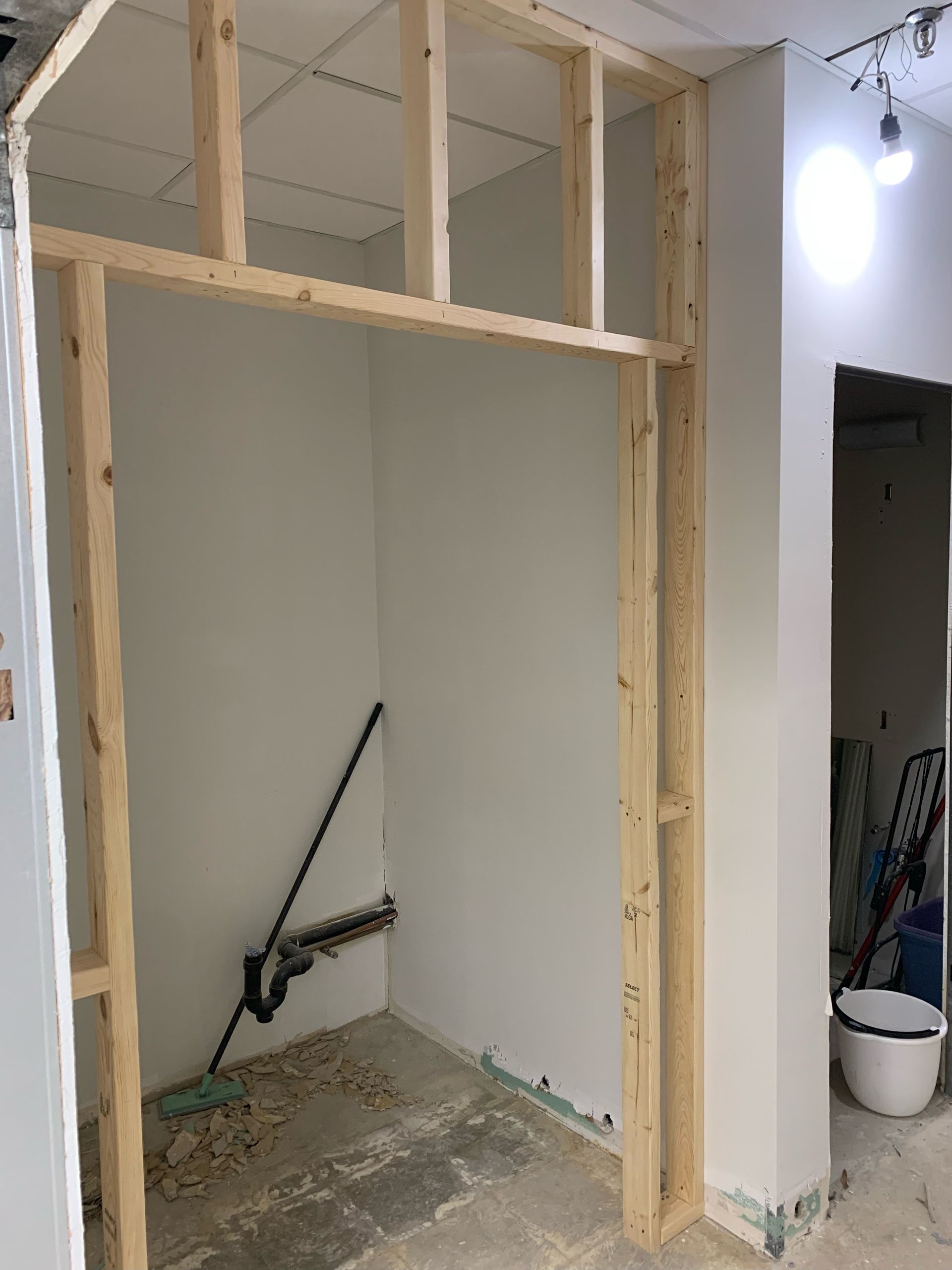Wooden frame construction in a room, doorway opening to a white-walled alcove.
