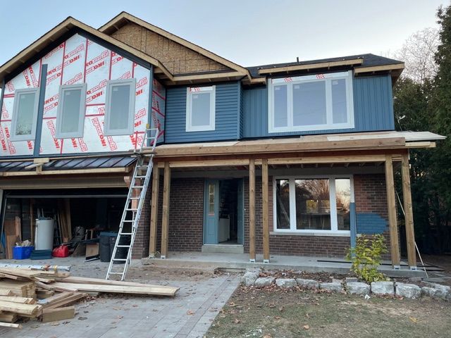 House under construction; blue siding, exposed wood framing, brick facade, windows, ladder.