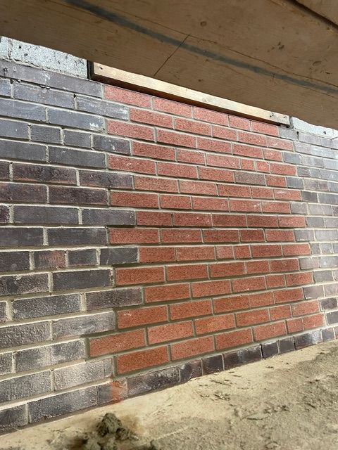 Brick wall with a section of red bricks surrounded by gray bricks. Construction site.