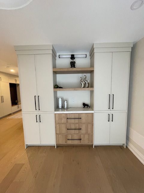 Built-in cabinets in a room with hardwood floors. Cream-colored upper cabinets flank a shelf and drawers.