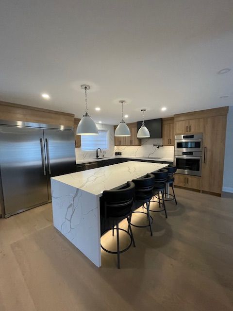Modern kitchen with white island, stainless steel appliances, wood cabinets, and black bar stools.