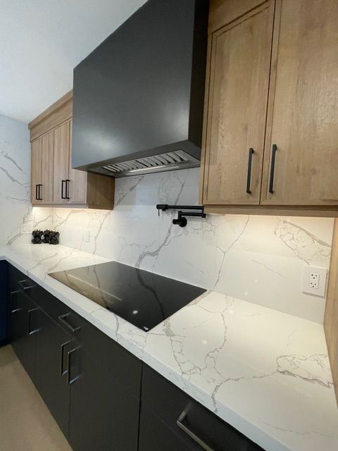 Modern kitchen with wood cabinets, black hood, white countertops, and black cooktop.