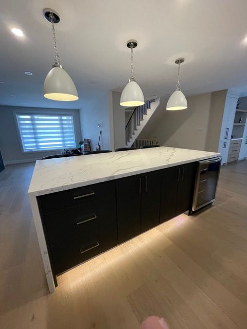 Kitchen island with white countertop, dark cabinets, and pendant lights.