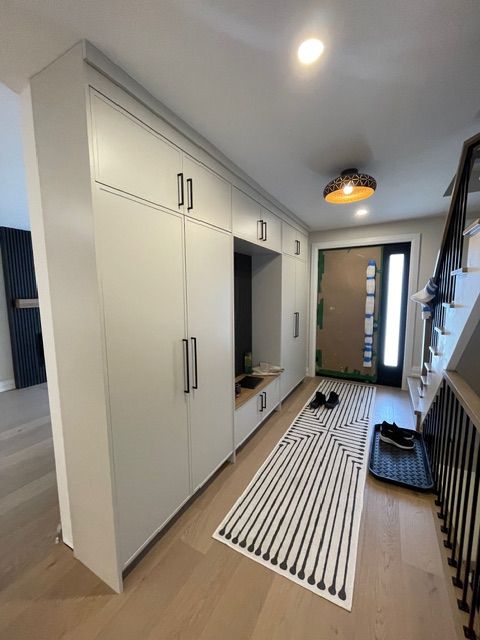 Gray built-in storage unit in a hallway with a bench, a striped rug, and a front door.
