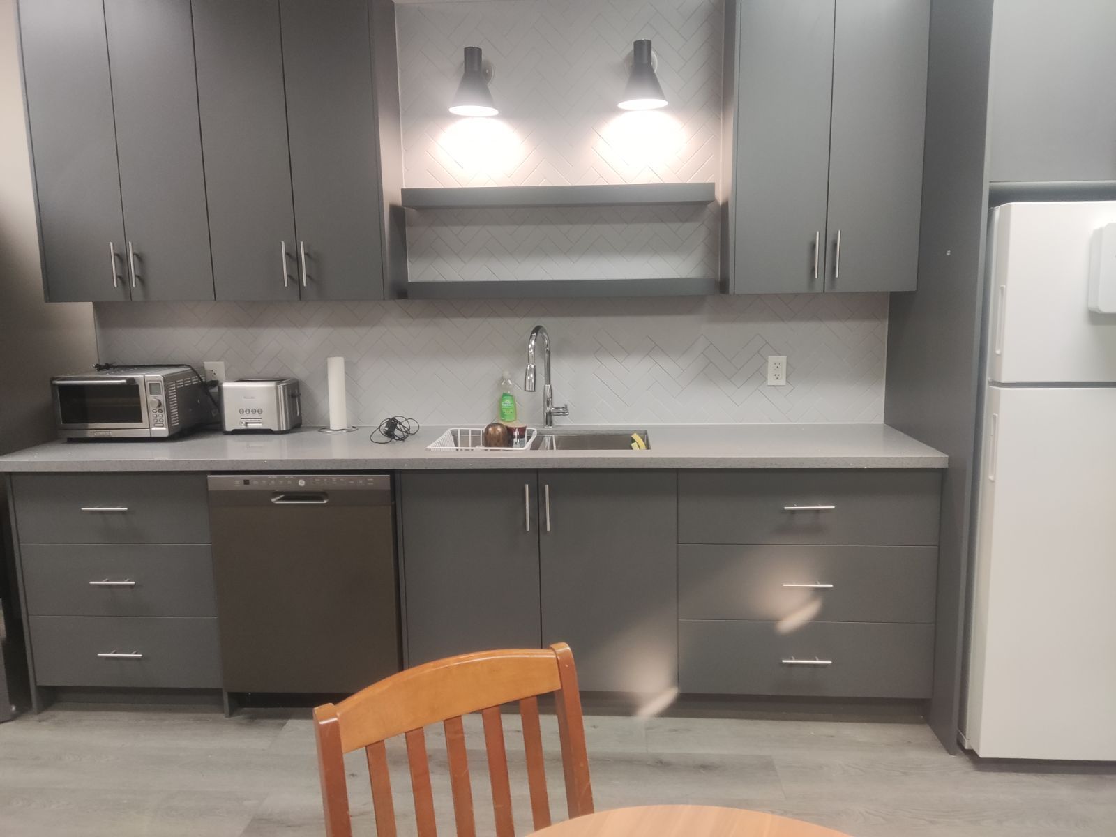 Gray kitchen with cabinets, sink, and appliances; a wooden chair in the foreground.