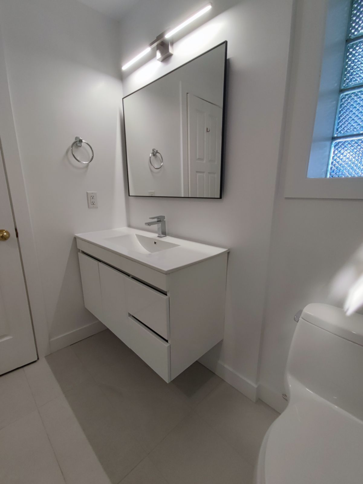 Modern white bathroom with floating vanity, mirror, and toilet.