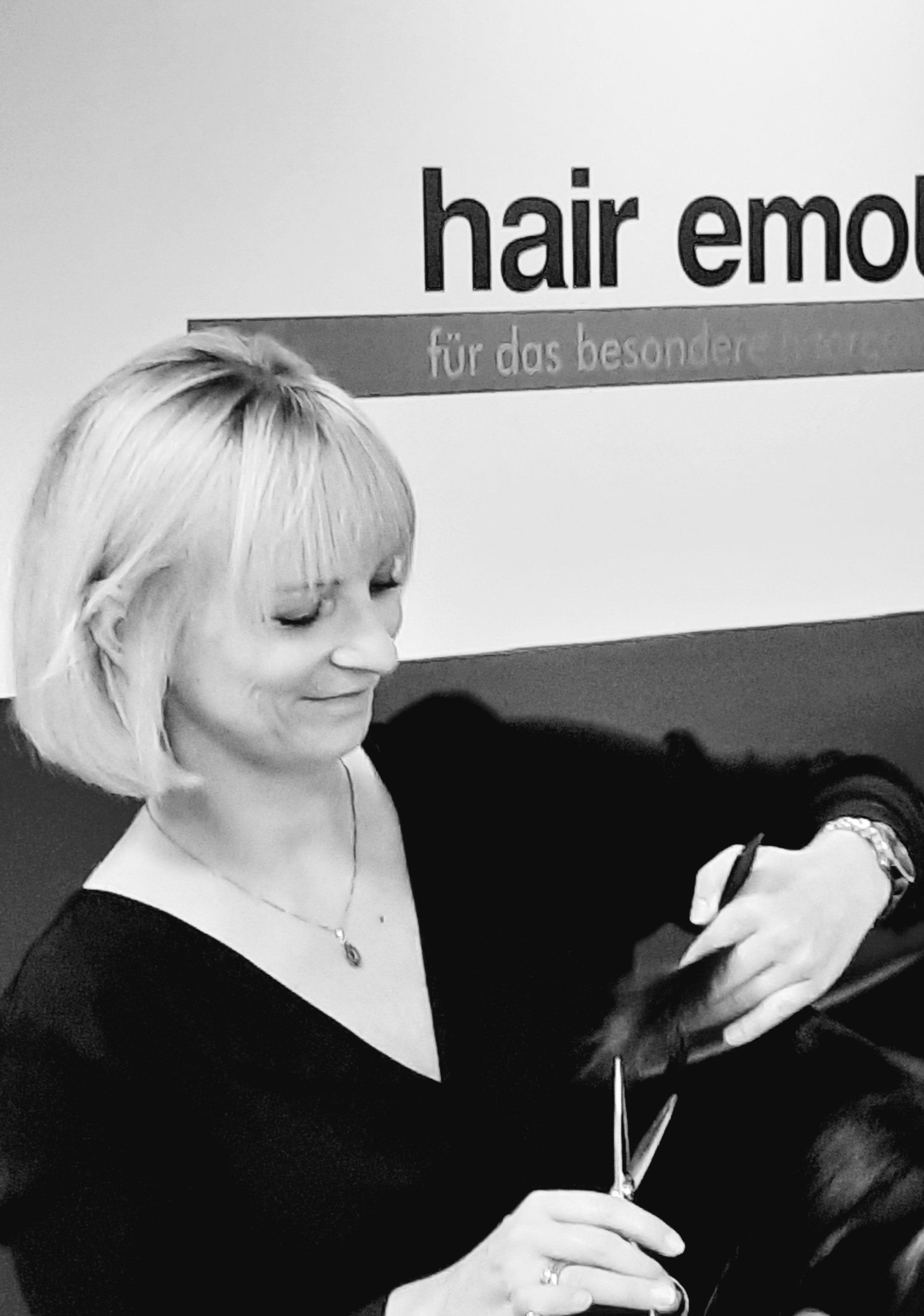 Eine Frau schneidet sich die Haare vor einem Schild mit der Aufschrift „Haaremotion“
