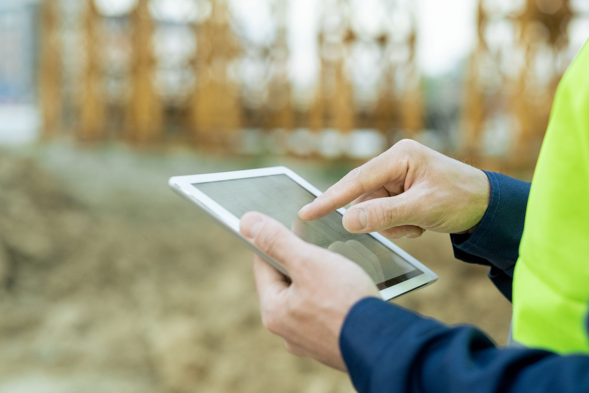 Person using a tablet at a construction site, wearing a yellow safety vest