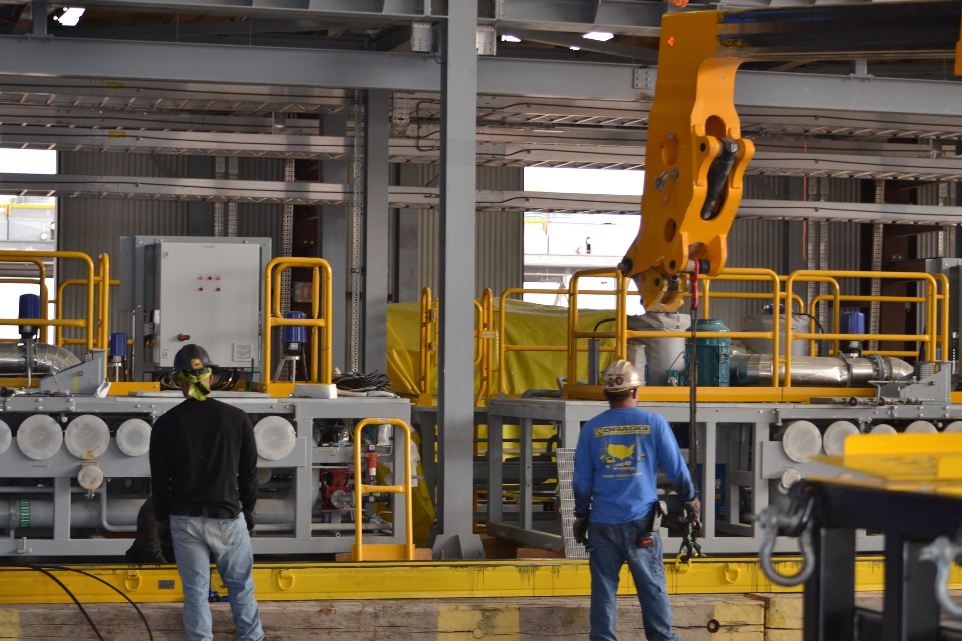 Workers in a factory stand near machinery while a yellow industrial robot arm operates overhead.