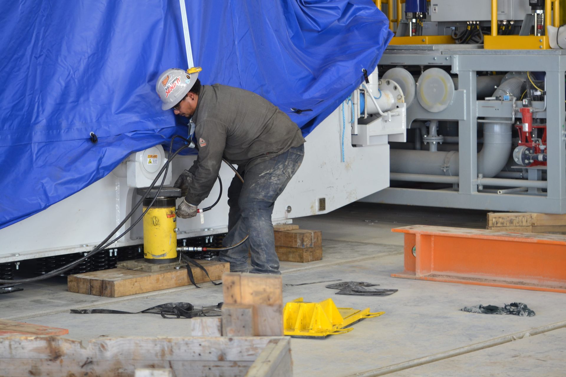 Worker adjusting equipment beside a large blue-covered machine in an industrial setting