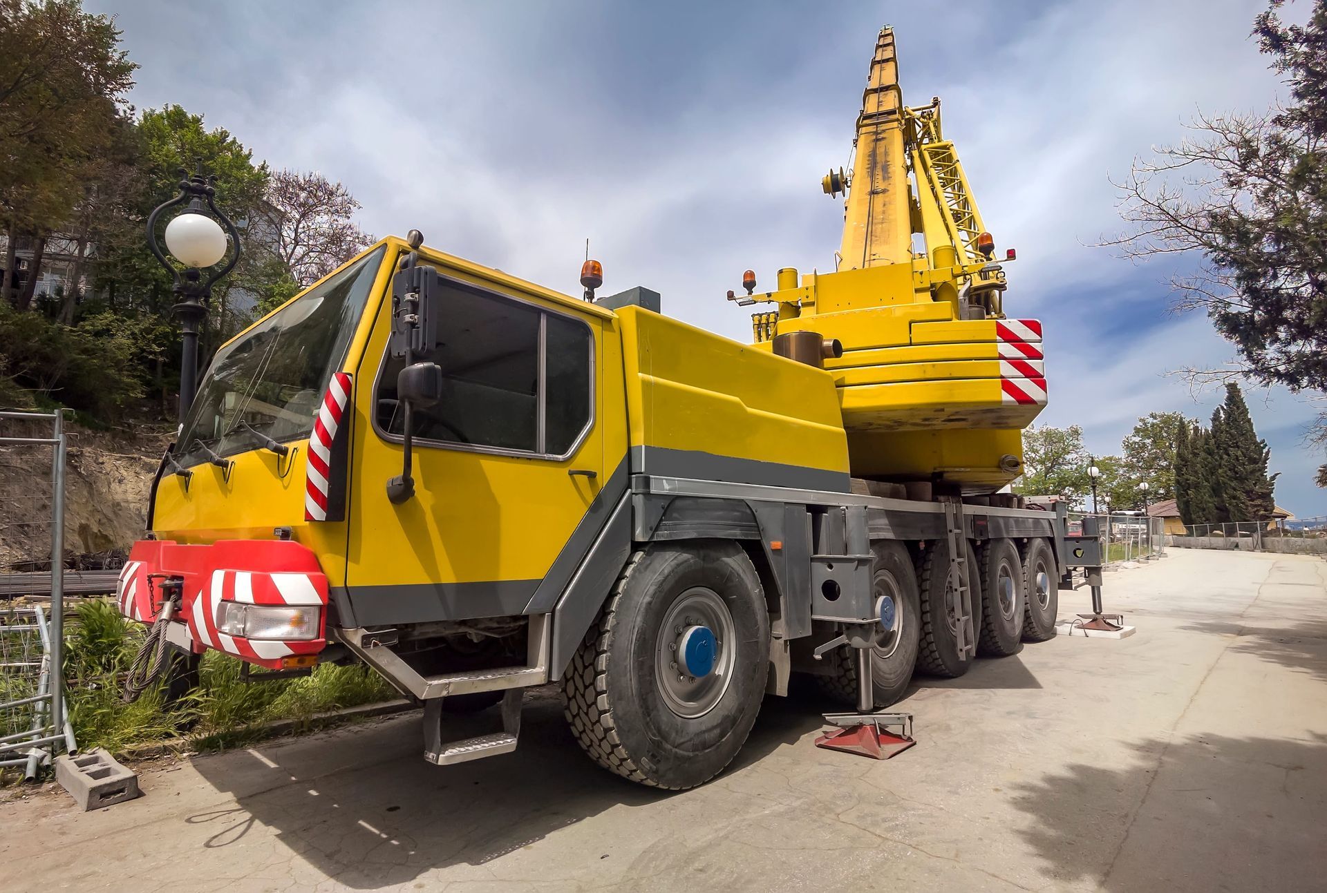 Yellow crane truck parked on a road, with trees and buildings in the background.