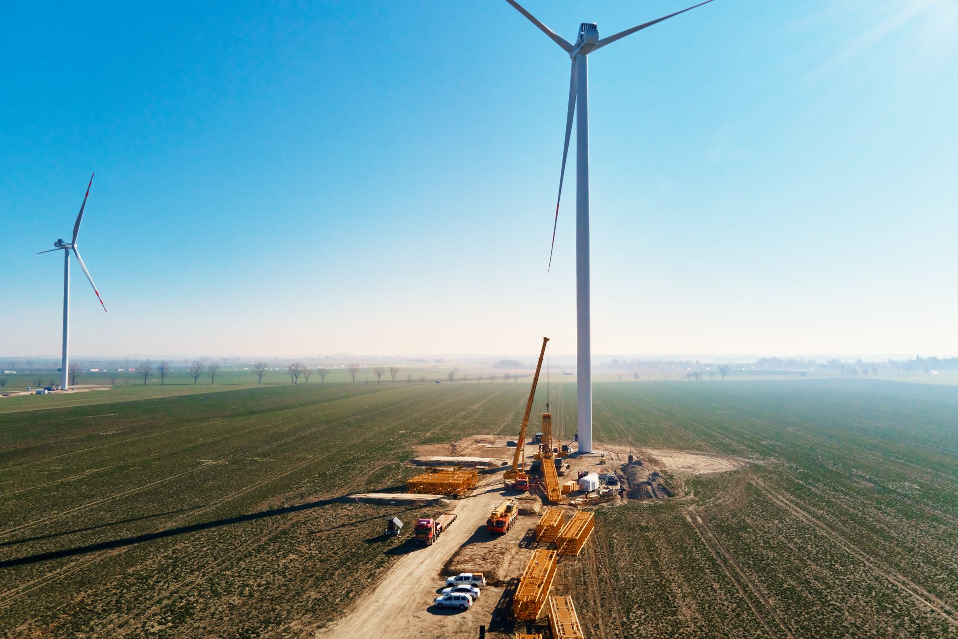 Wind turbines under construction in a flat green field under a clear blue sky.