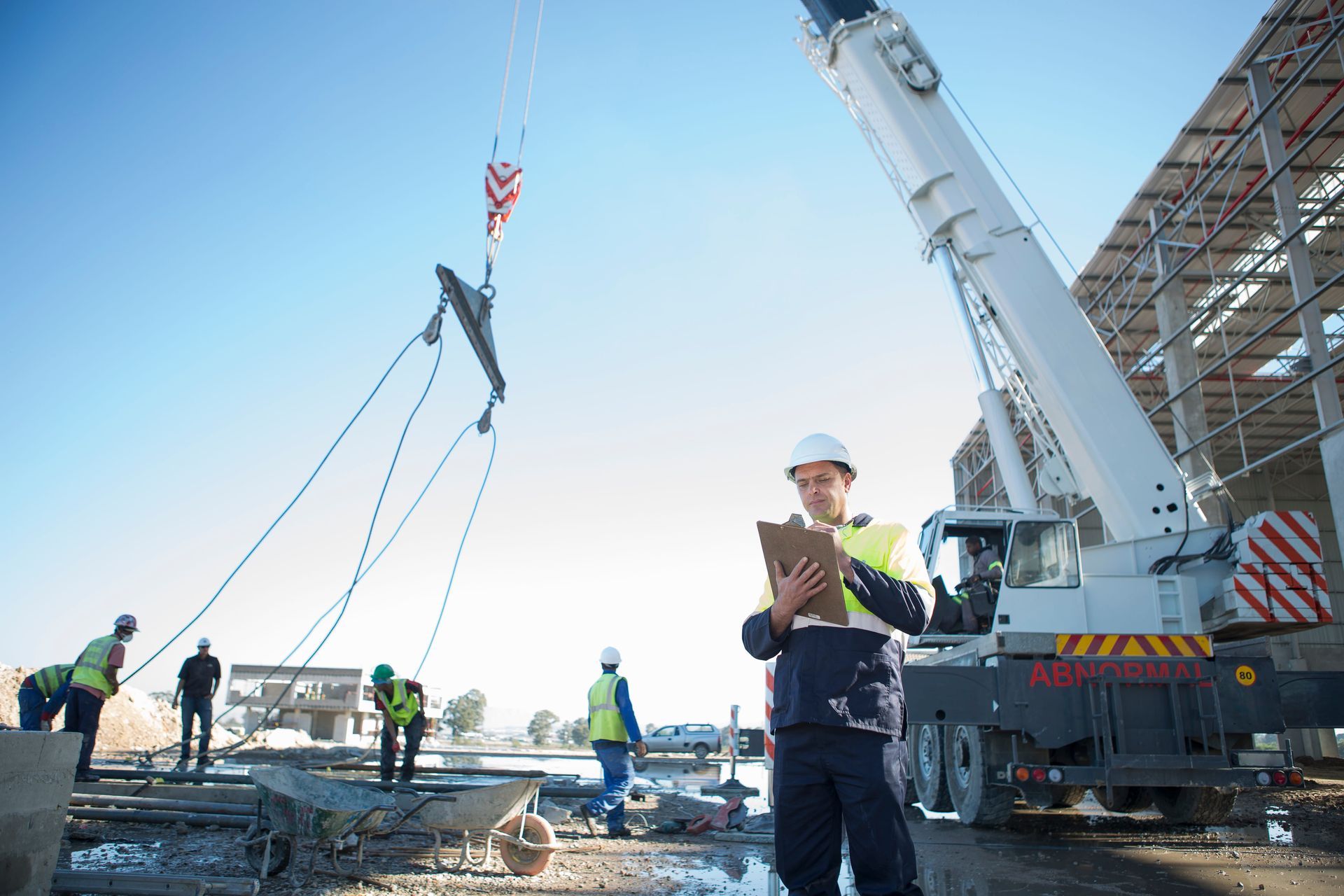 Construction crew lifting materials with a crane at a building site, worker in hard hat in foreground.
