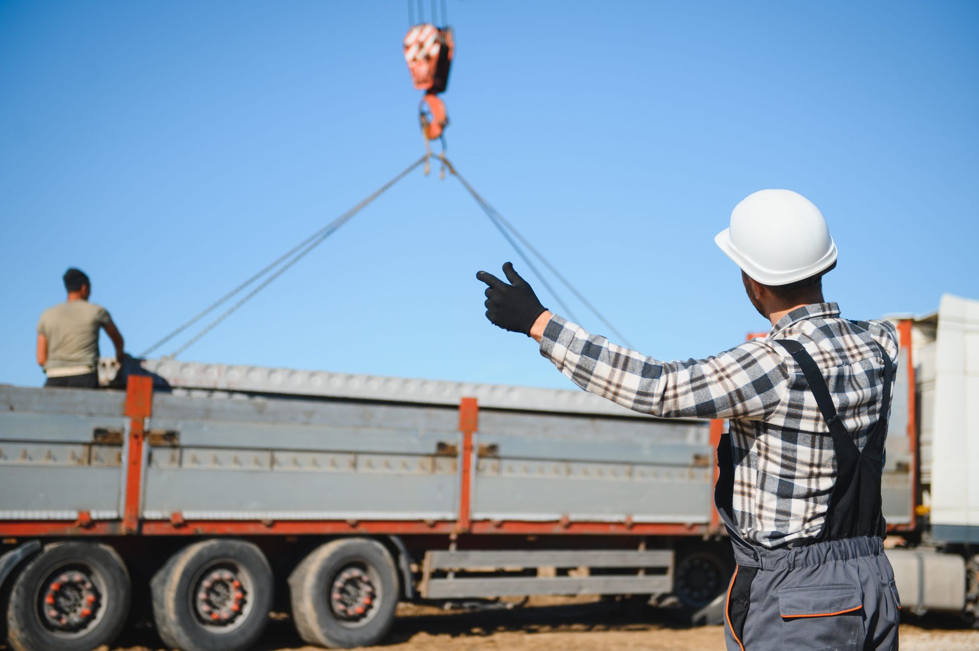 Workers guiding a crane lifting a load onto a flatbed truck under a blue sky