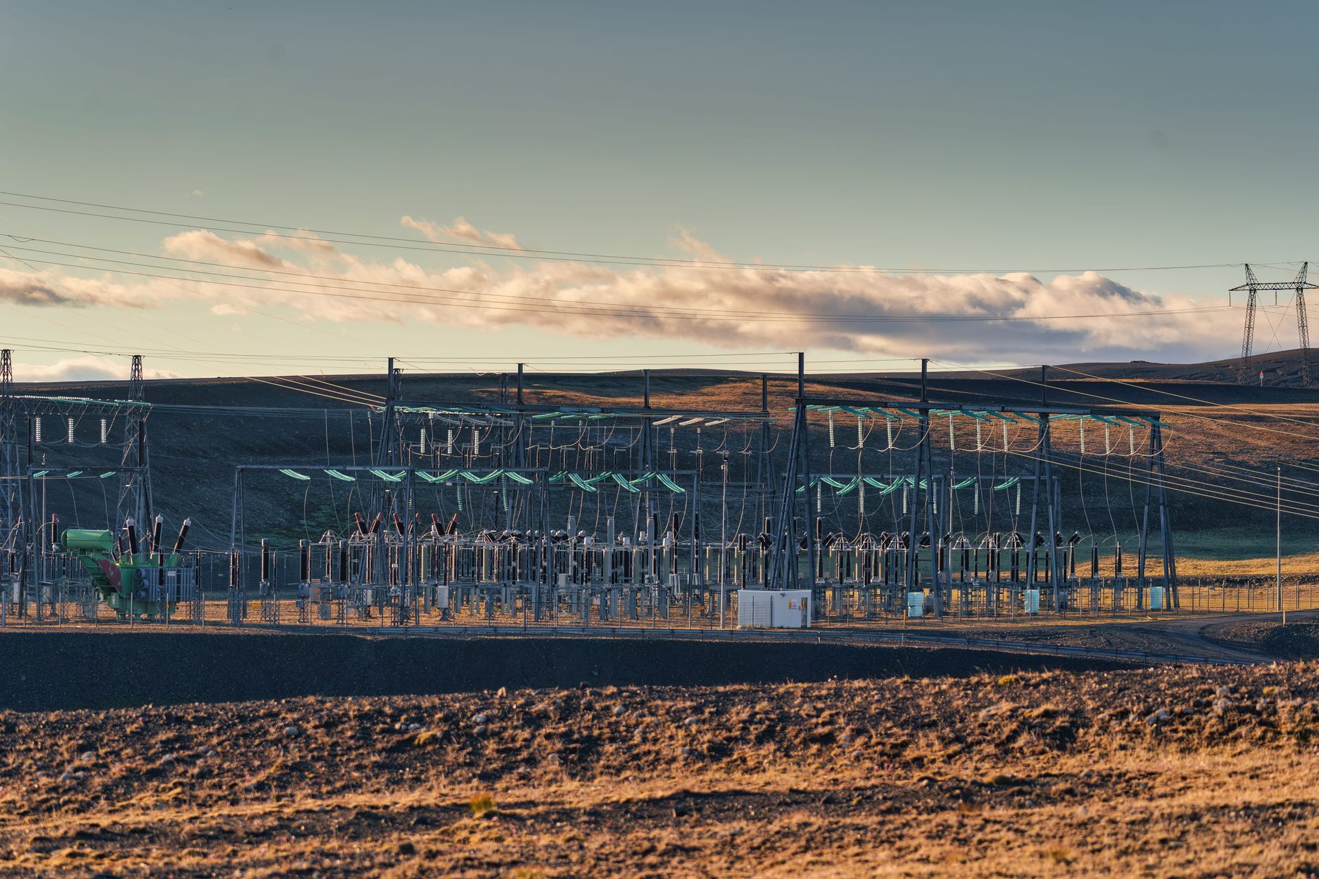 Industrial solar farm in a barren field at sunset, with rows of panels and distant mountains under a cloudy sky