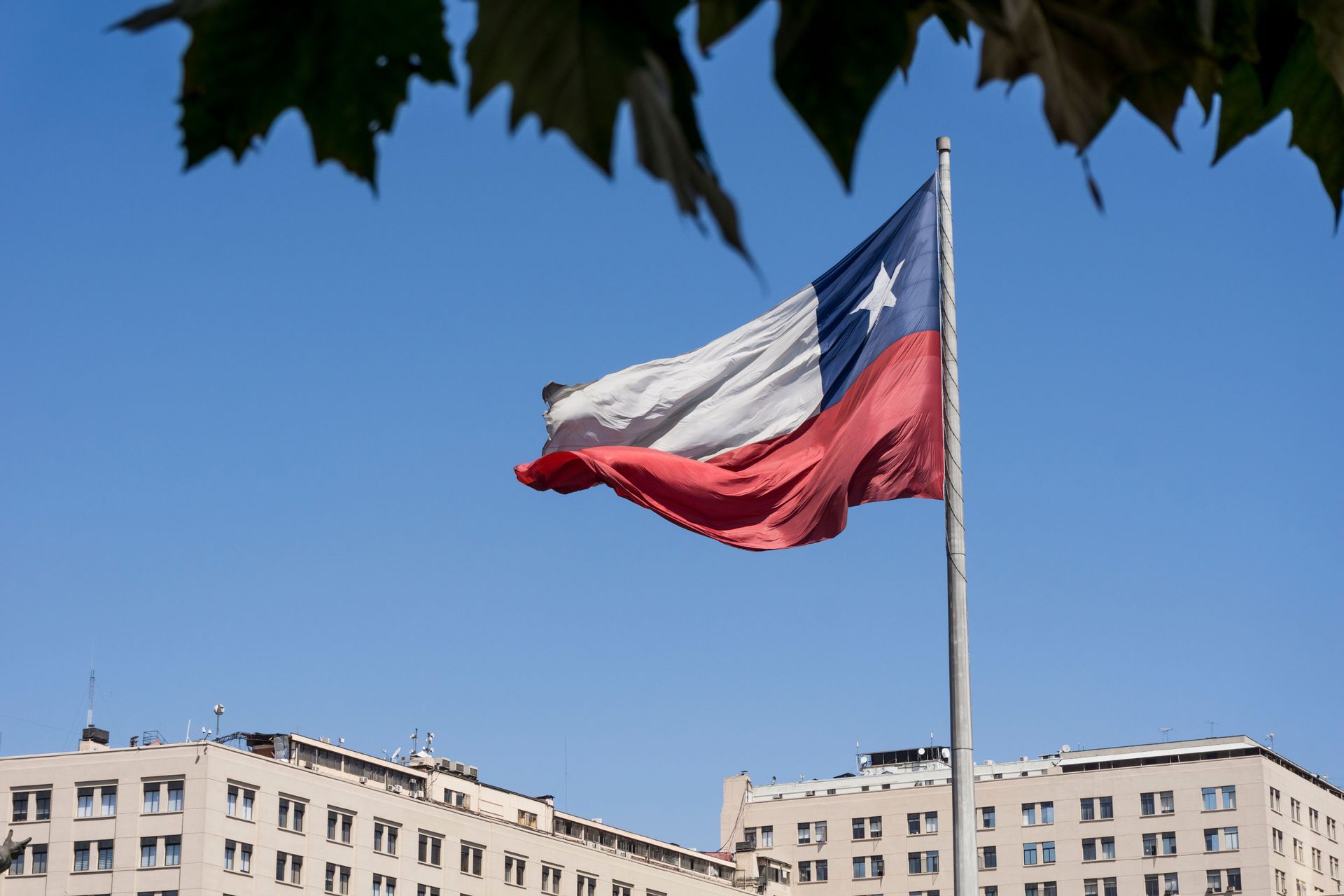 Chilean flag waving on a pole above buildings against a clear blue sky
