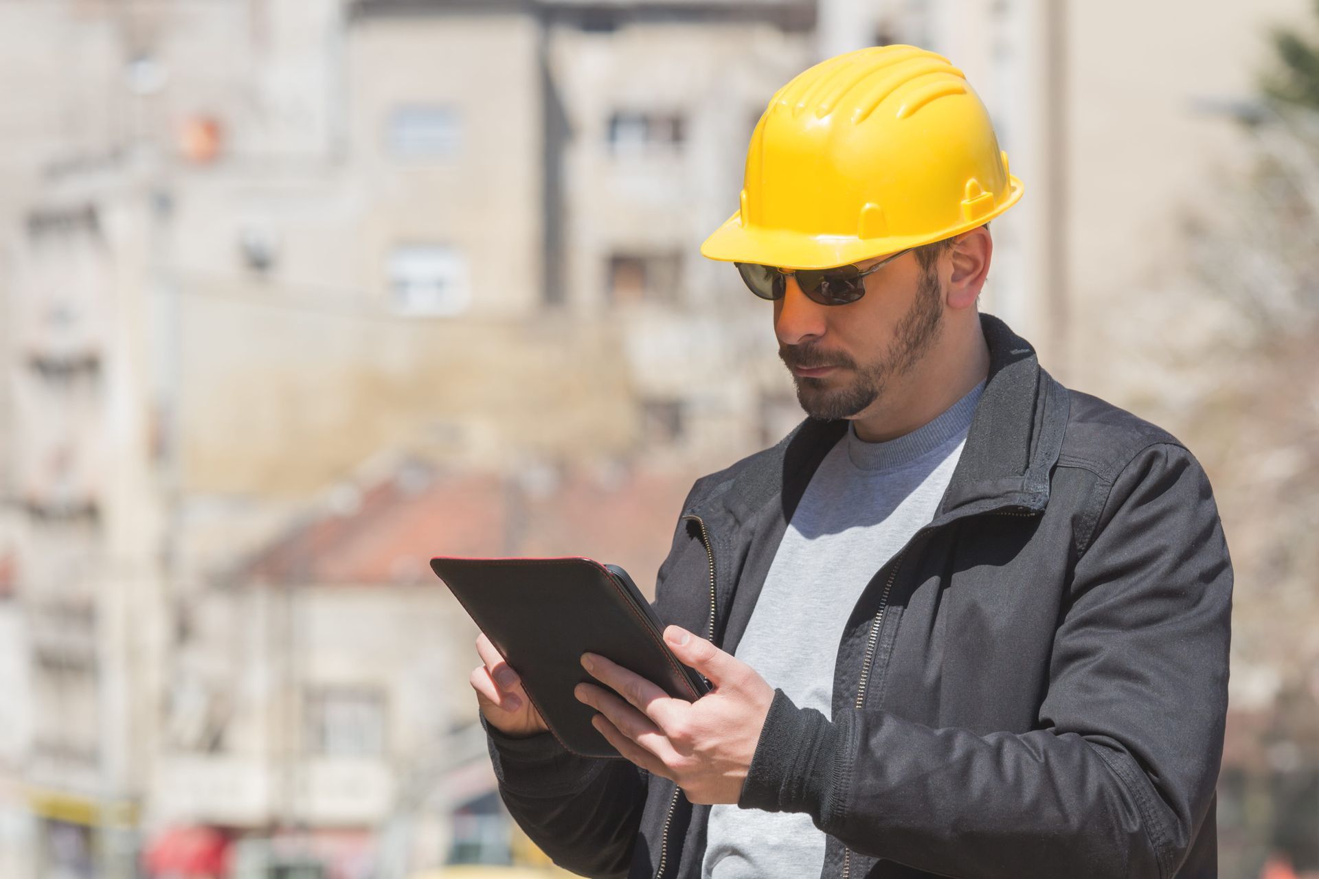 Construction worker in yellow hard hat using a tablet on a job site