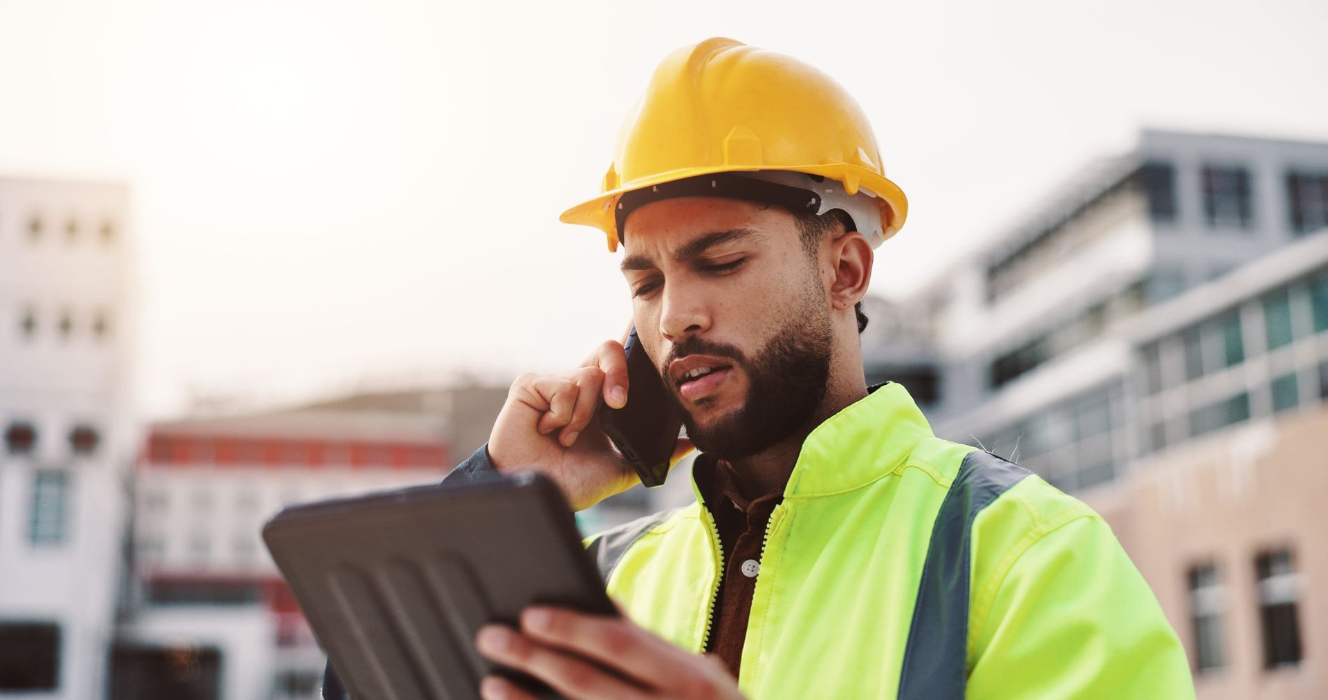 Construction worker in yellow hard hat and safety vest using a tablet at a building site