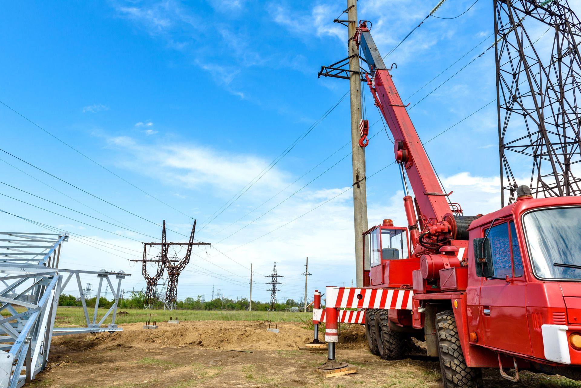 Red crane truck working on power lines in a grassy field under a blue sky