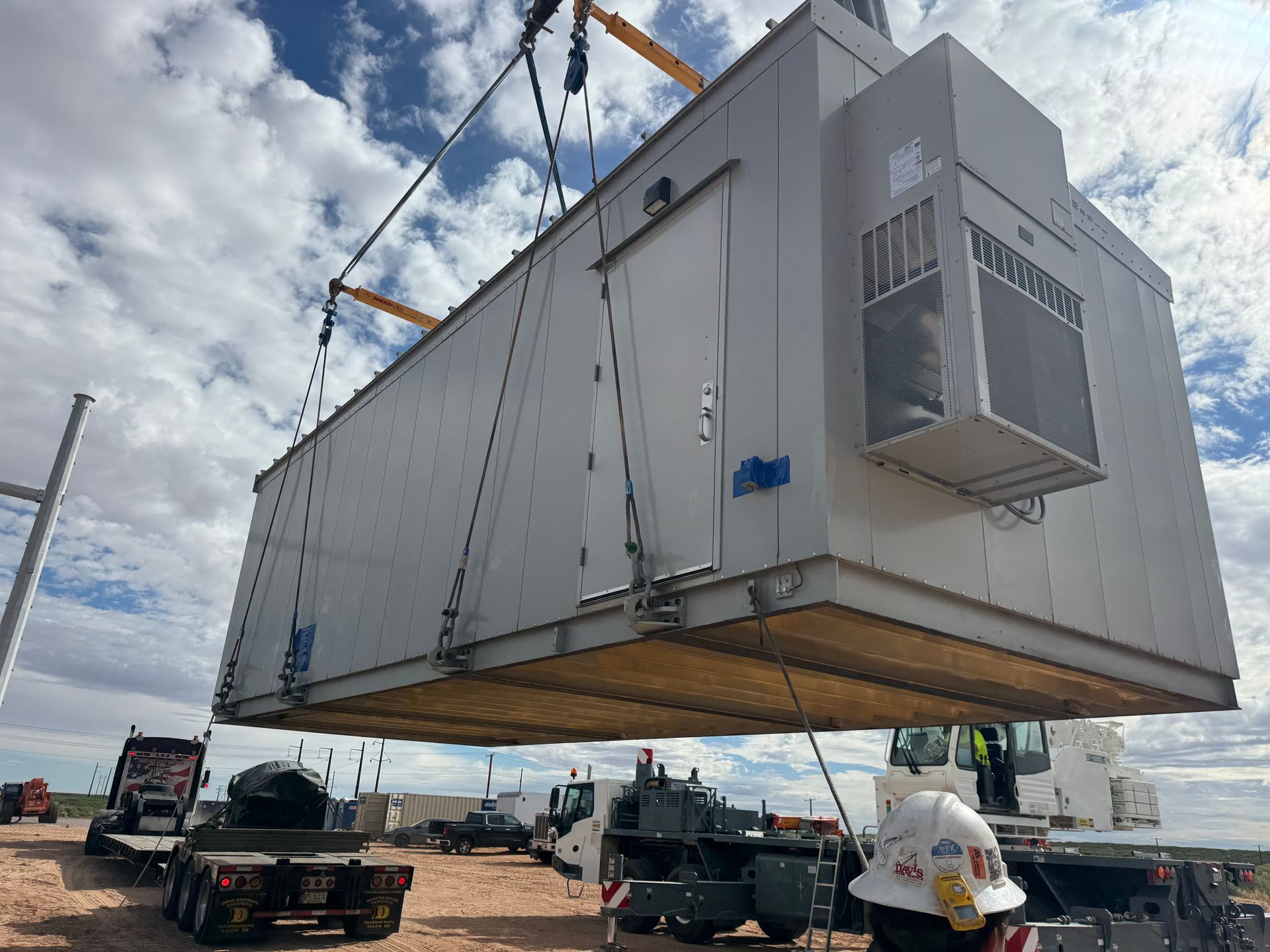 Large modular building section being lifted by cranes onto transport trailers in an industrial yard