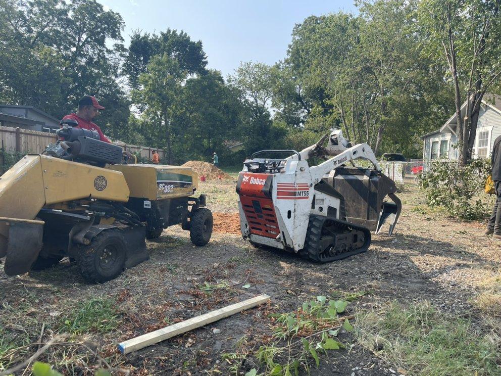 A man is driving a stump grinder next to a smaller machine.