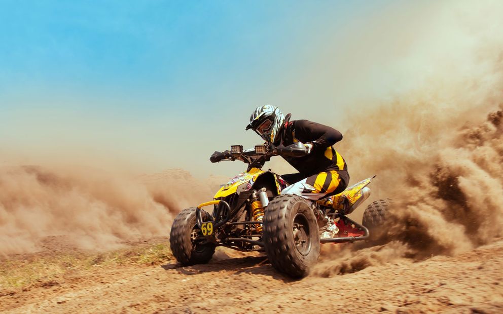 Un pilota di quad sbanda su un terreno polveroso, sollevando una grande nuvola di sabbia.