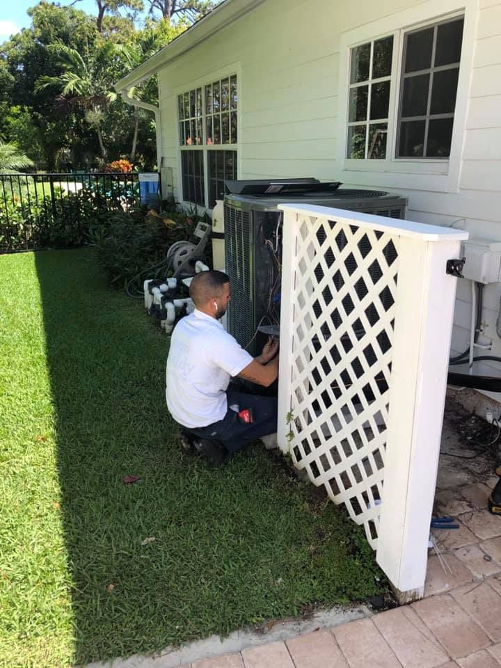 Man working on an AC unit outdoors next to a house, with white lattice.