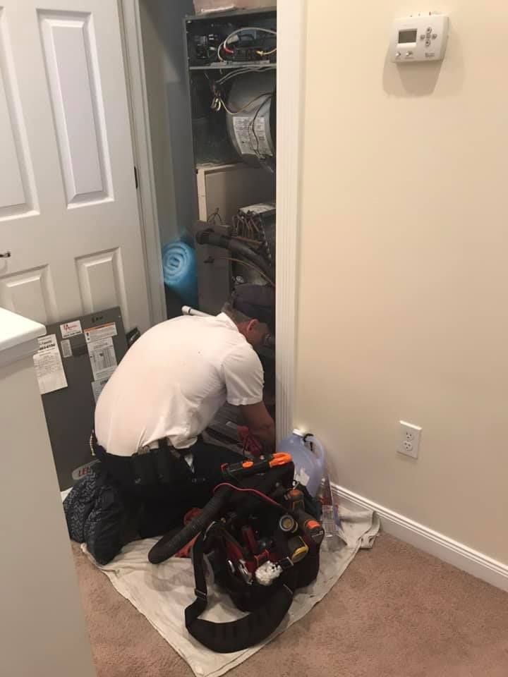 A person in white shirt working on equipment inside a utility closet. Tool bag on floor.