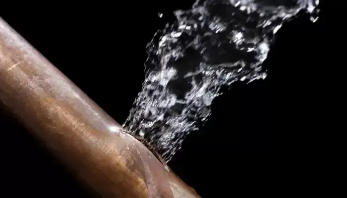 Water spurts forcefully from a hole in a copper pipe against a black background.