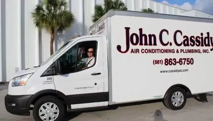 White John C. Cassidy HVAC truck with a person driving; parked in front of a building.