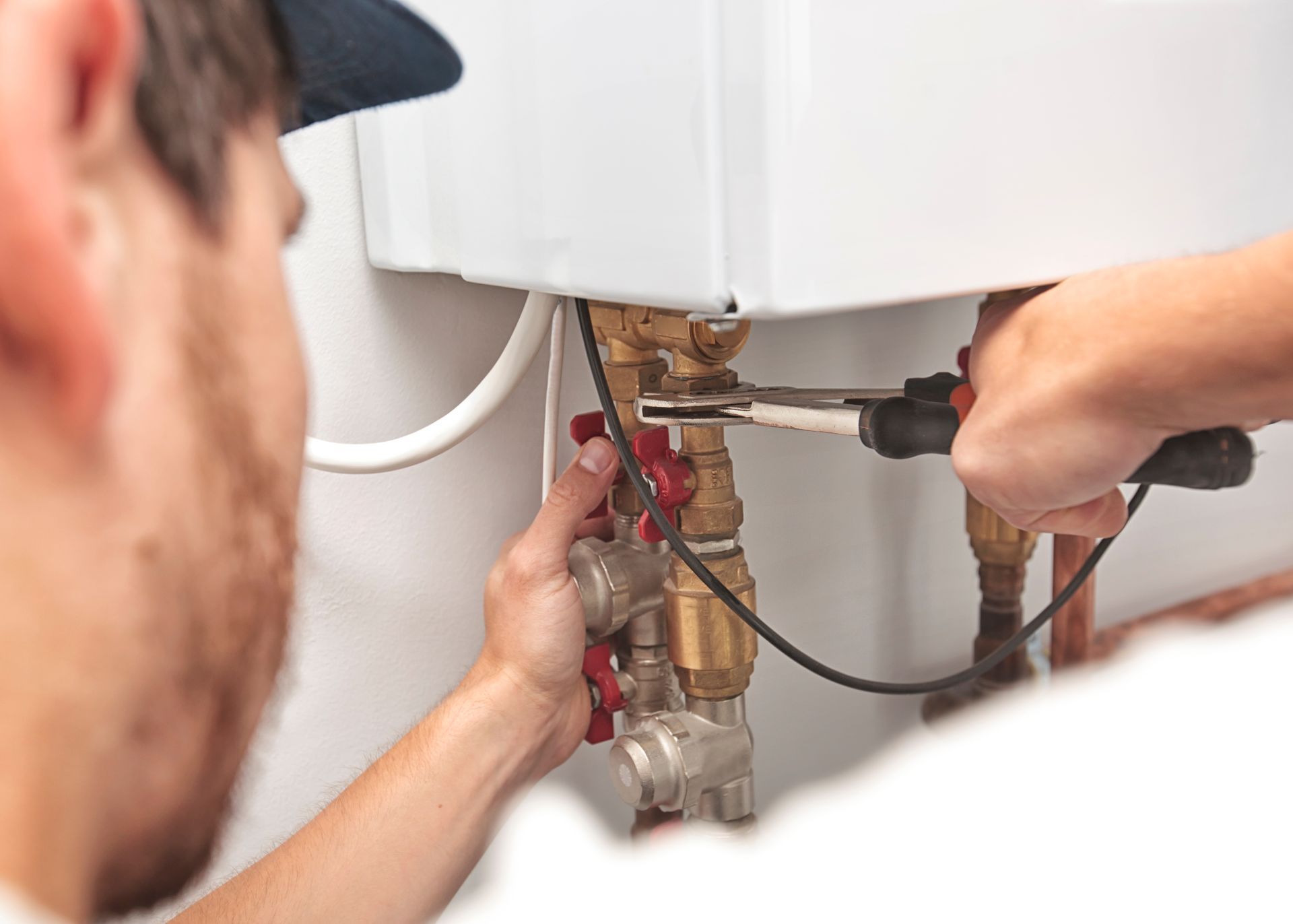 Plumber using a wrench to repair pipes near a white appliance.