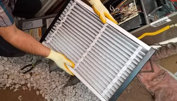 Person in gloves holding a new HVAC air filter, near wires and insulation.
