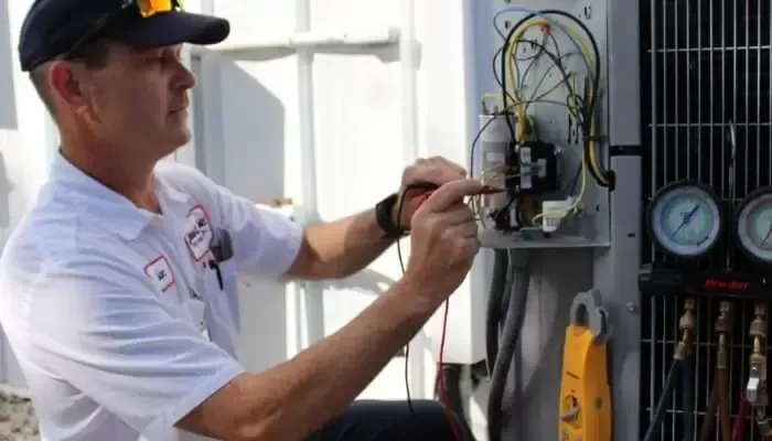HVAC technician working on outdoor air conditioning unit, using tools and gauges.