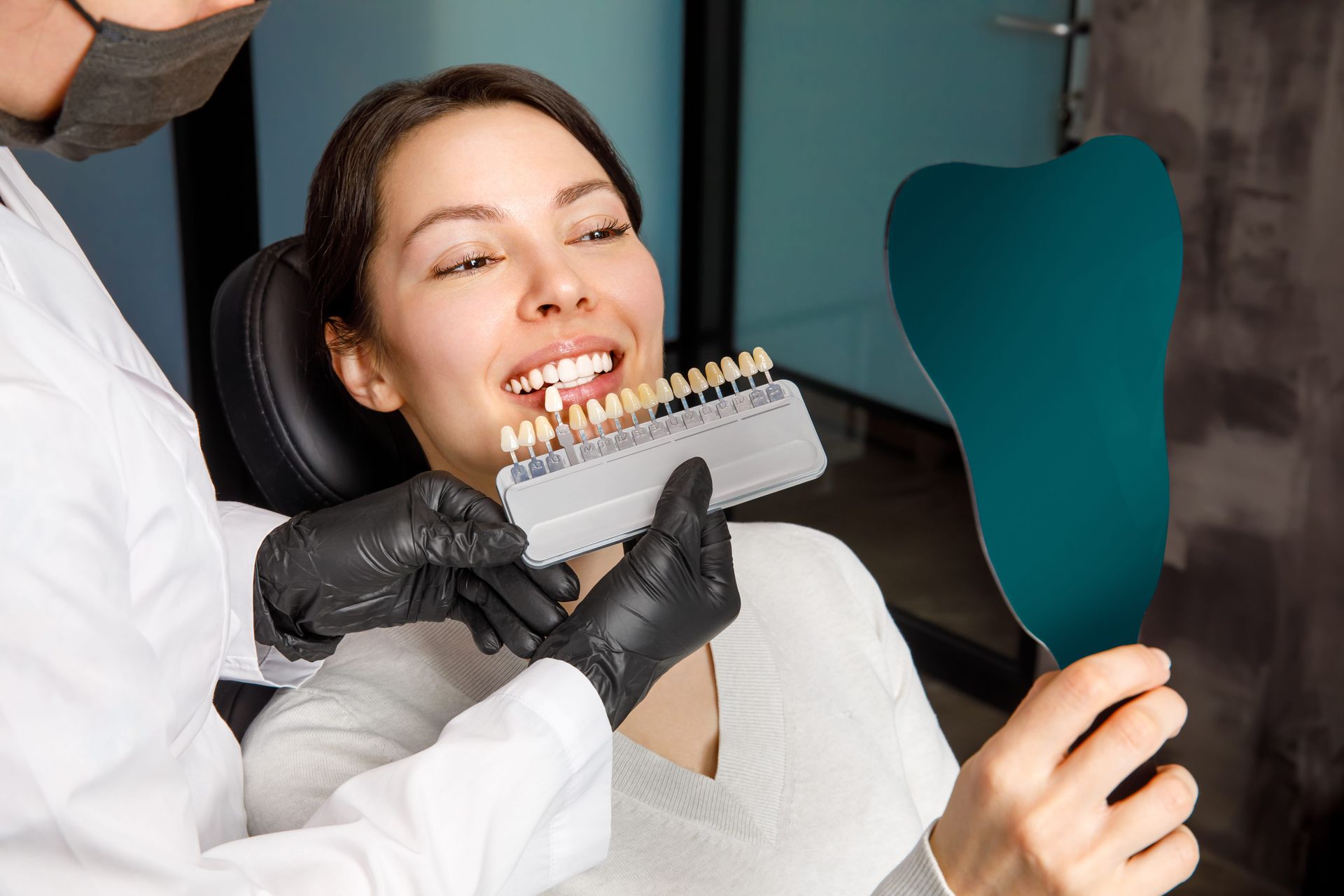 Dentist matching teeth shade with a shade guide for a smiling patient in a clinic.