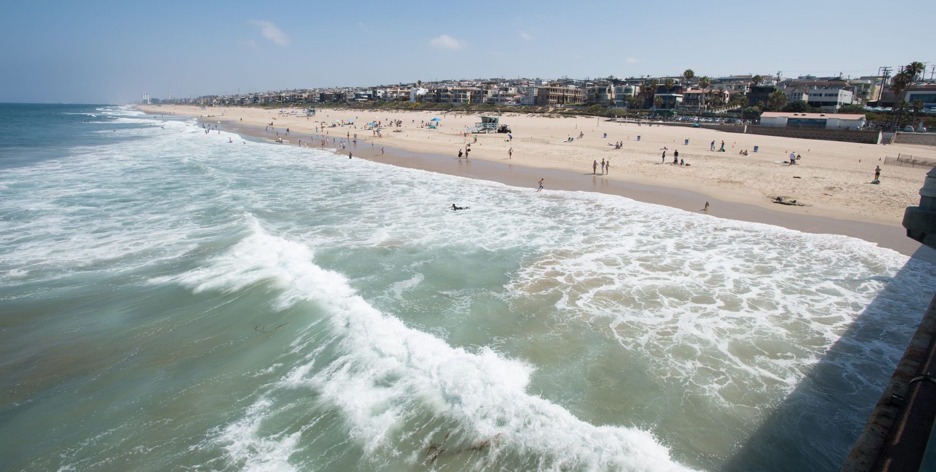 Sunny beach with waves rolling onto a crowded sandy shoreline and a coastal town in the distance