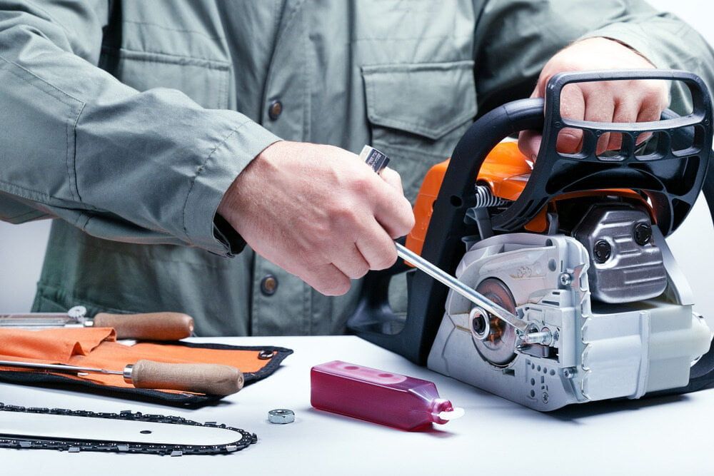 A Person in a Grey Shirt Uses a Wrench to Adjust a Chainsaw — Tuggerah Outdoor Power in Tuggerah, NSW