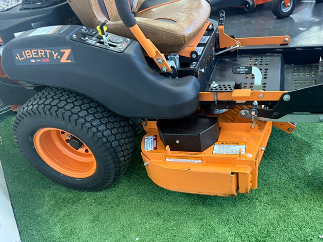 Orange zero-turn lawn mower on artificial grass, close-up side view