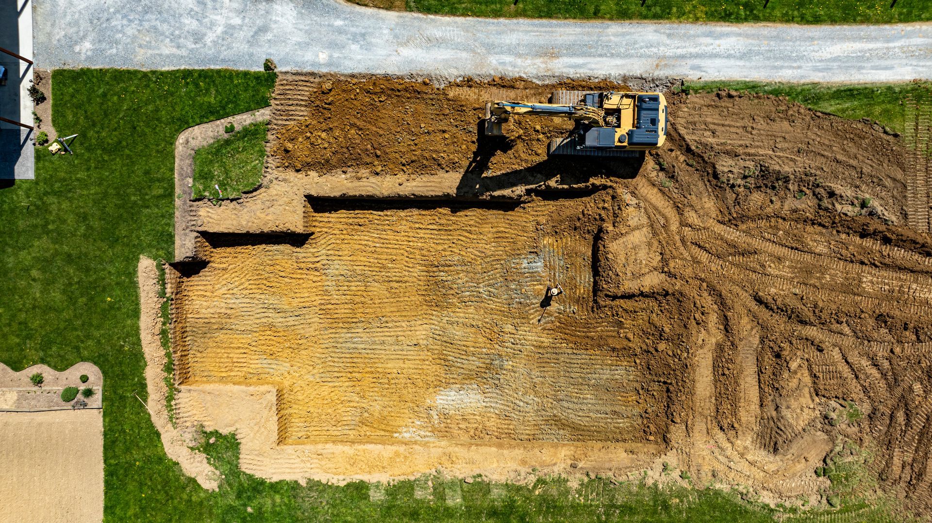 Aerial view of a construction site; excavator digging foundation for a building in a grassy area.